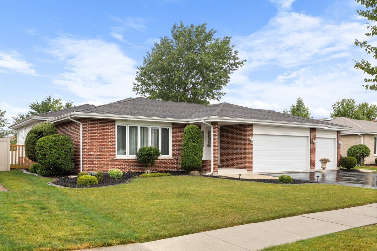 Suburban home with brick siding, neat landscaping, and wet blacktop driveway