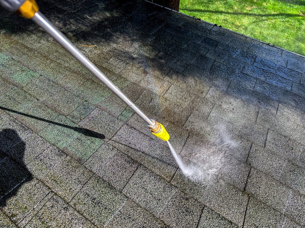 A pressure washer is being used to clean the roof of a house on a clear day.