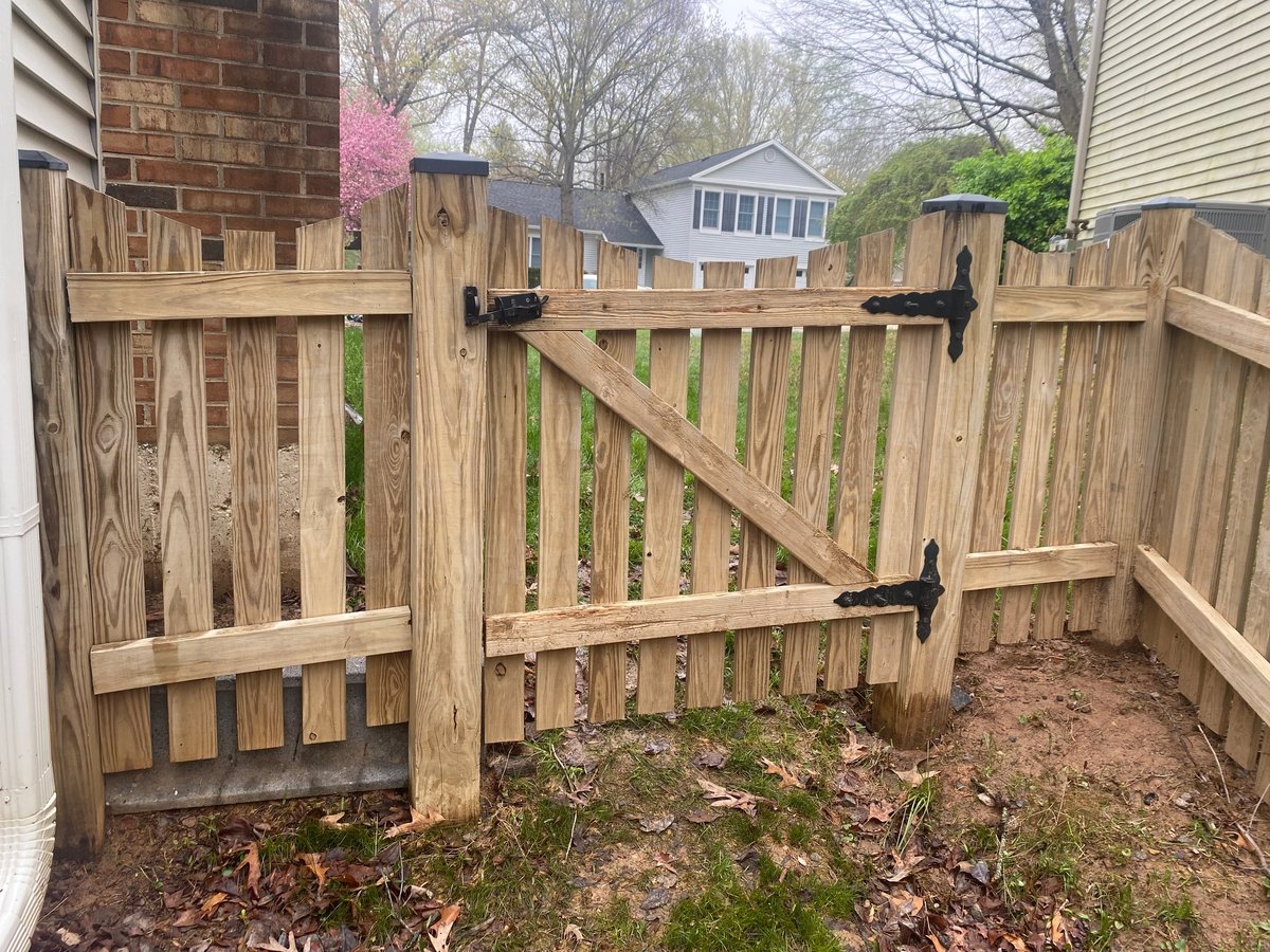 Wooden fence with gate in residential backyard, with trees and houses visible in background