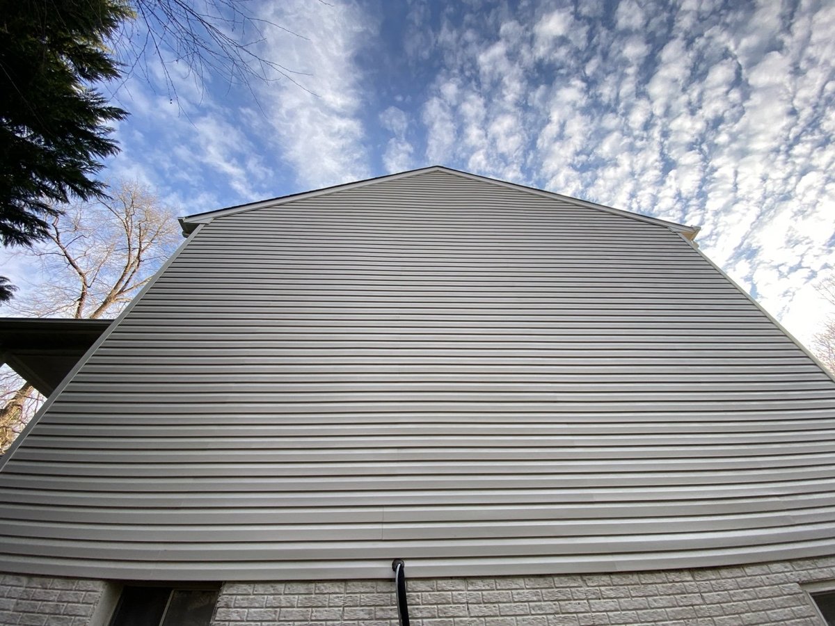 Modern barn with curved metal roof and stone foundation under partly cloudy blue sky