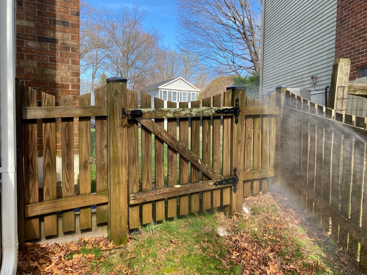 Wooden fence gate in backyard with houses and bare trees visible in background on clear day